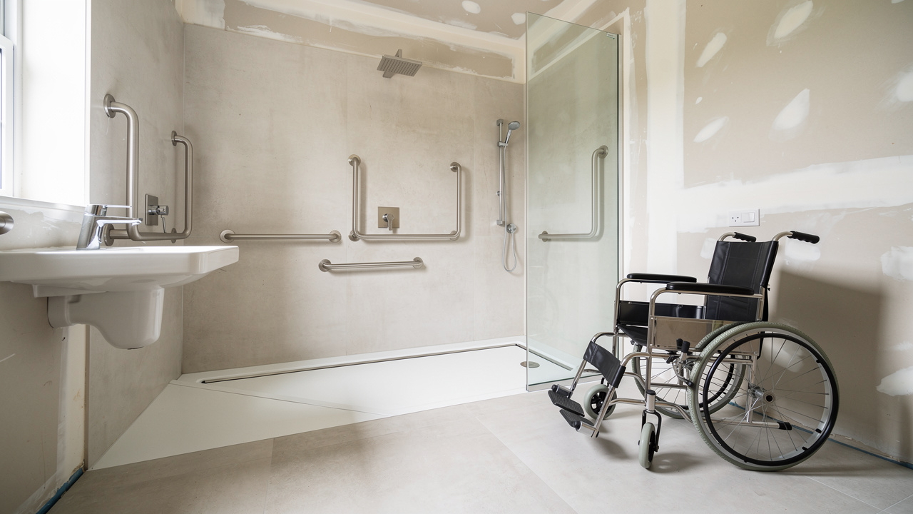Salle de bains accessible en cours d’aménagement avec douche de plain-pied, barres d’appui, lavabo suspendu et espace dégagé pour la rotation d’un fauteuil roulant.